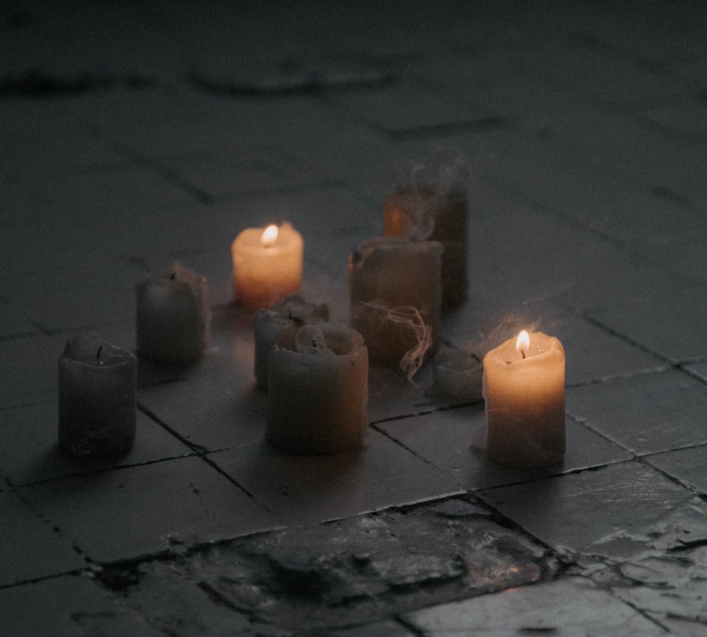 A serene scene of candles burning on a dark tiled floor with smoke.