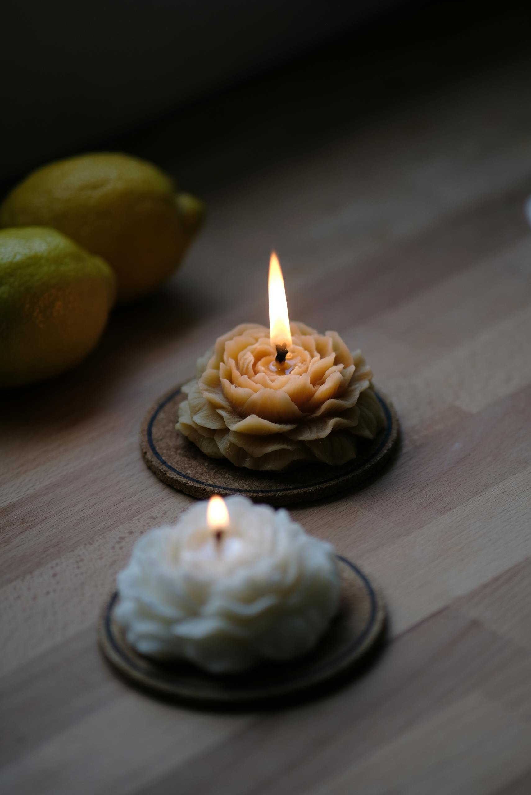 Two flower-shaped candles lit on a wooden table with lemons, creating a cozy ambiance.