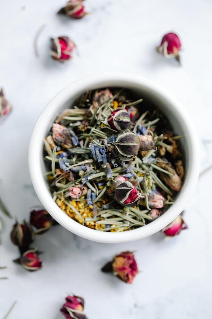 A close-up top view of a bowl filled with a herbal tea blend of dried roses and lavender.