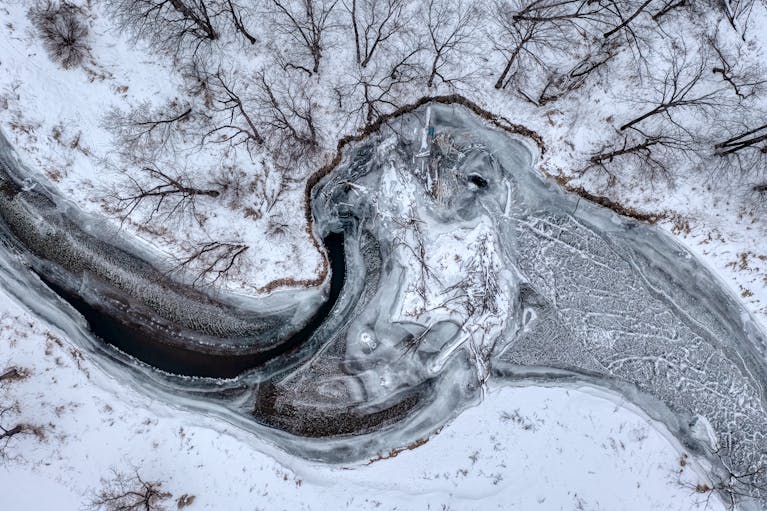 Aerial shot of a frozen river winding through a snow-covered winter landscape representing freeze and sadness instead of flow