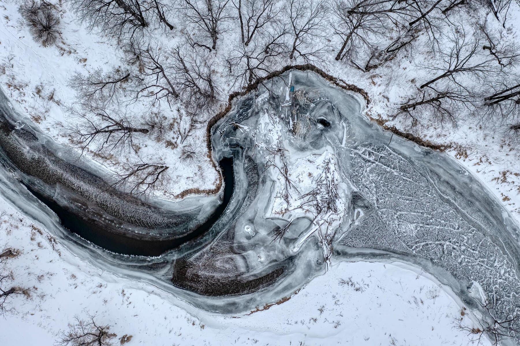 Aerial shot of a frozen river winding through a snow-covered winter landscape representing freeze and sadness instead of flow